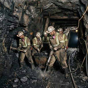 Five coal miners wearing helmets with lights and safety vests working inside a mine tunnel